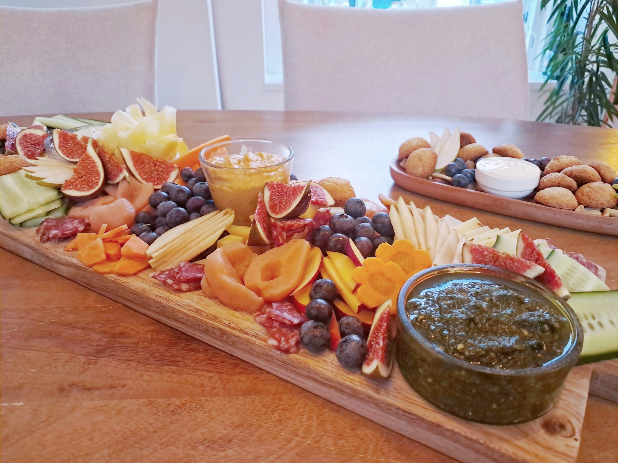 Houten plank vol vijgen, blauwe bessen, peer, worst, kaas en dips op een gedekte tafel
